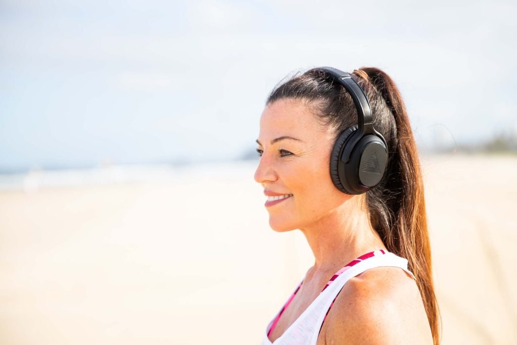 Woman wearing over-the-ear headphones and smiling at the beach.