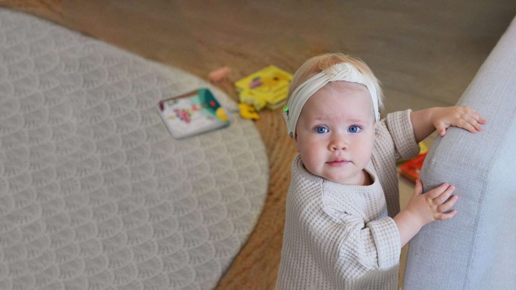 Young child standing by a grey couch.