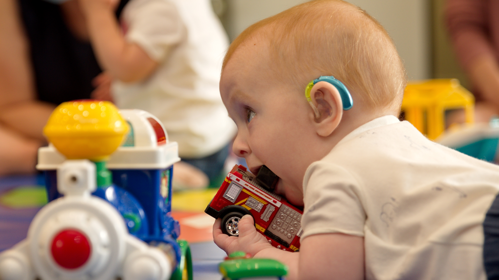 Baby with hearing aid chewing on a toy fire engine at play group.