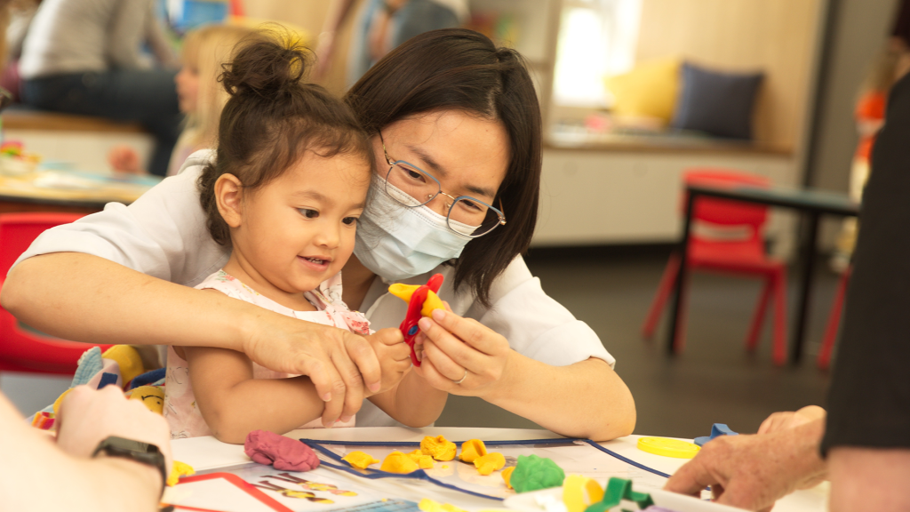 Mum and young daughter cutting play dough with scissors.