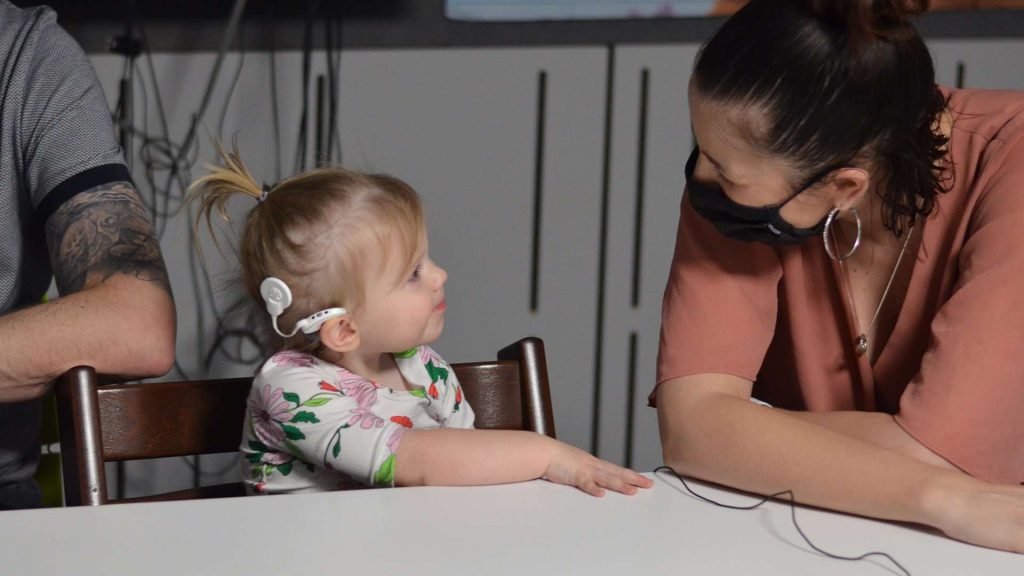 Child With Cochlear Implant Looking At Women In Mask