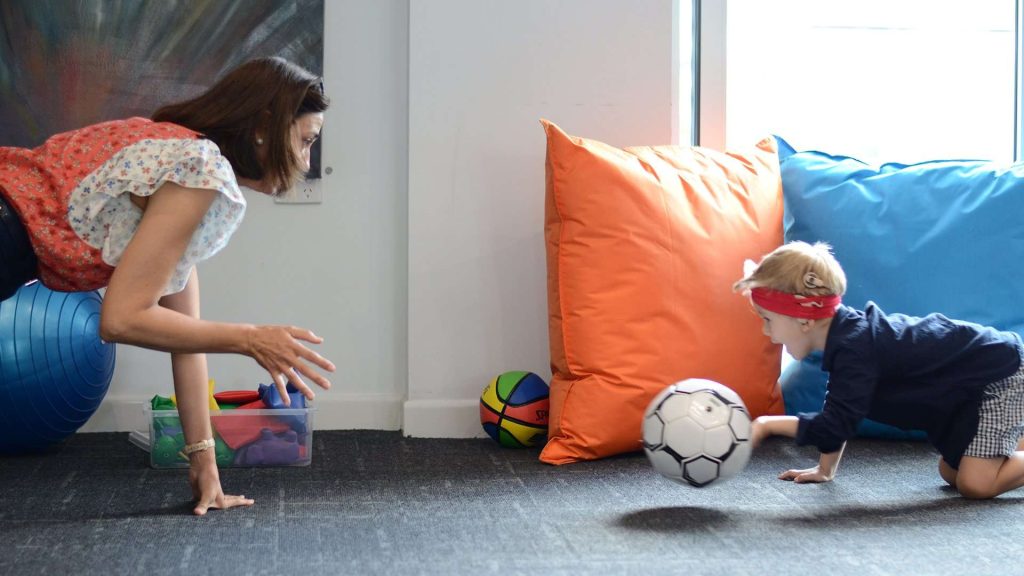 Occupational therapist and young boy playing with a soccer ball.