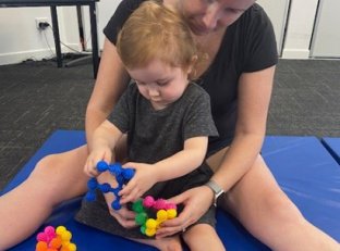 Img Lady Sitting With Girl Between Her Legs Playing With Puzzle