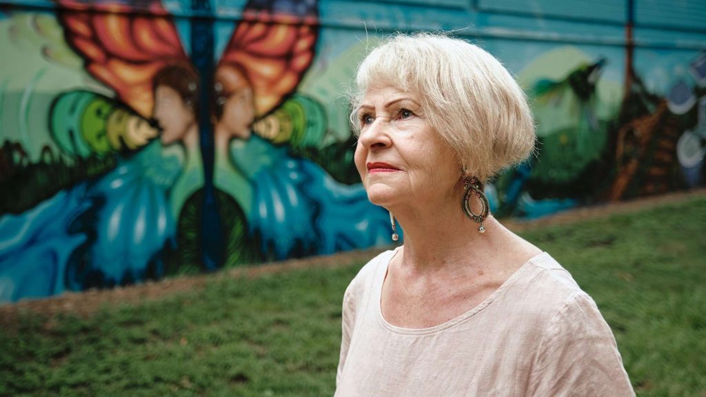 Lady with grey hair walking outdoors in front of a mural.