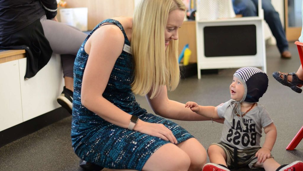 Speech pathologist kneeling down with young child.