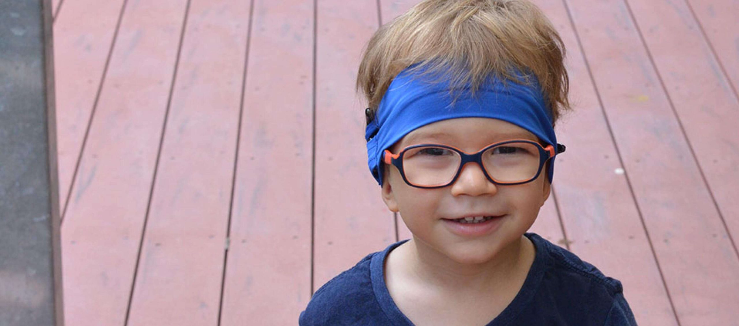 Boy with glasses wearing a blue cochlear implant headband.